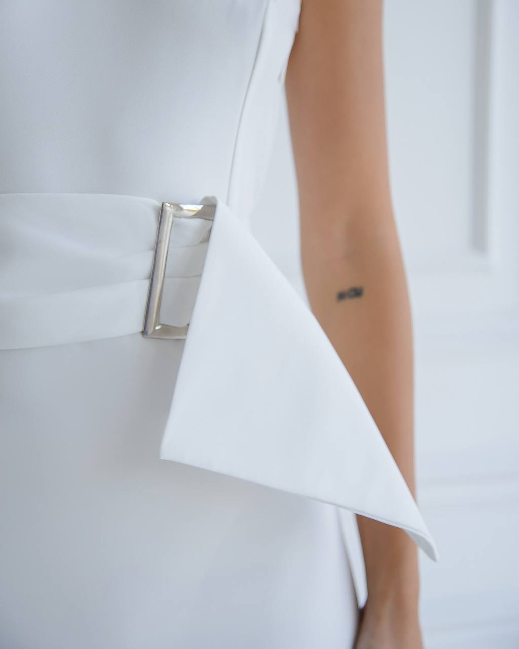 Close-up of a white dress with a silver clutch and tattoo detail.
