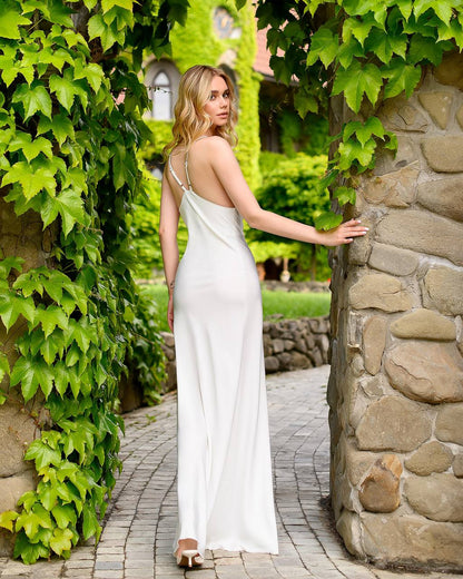 Woman in a white dress standing between stone walls and greenery