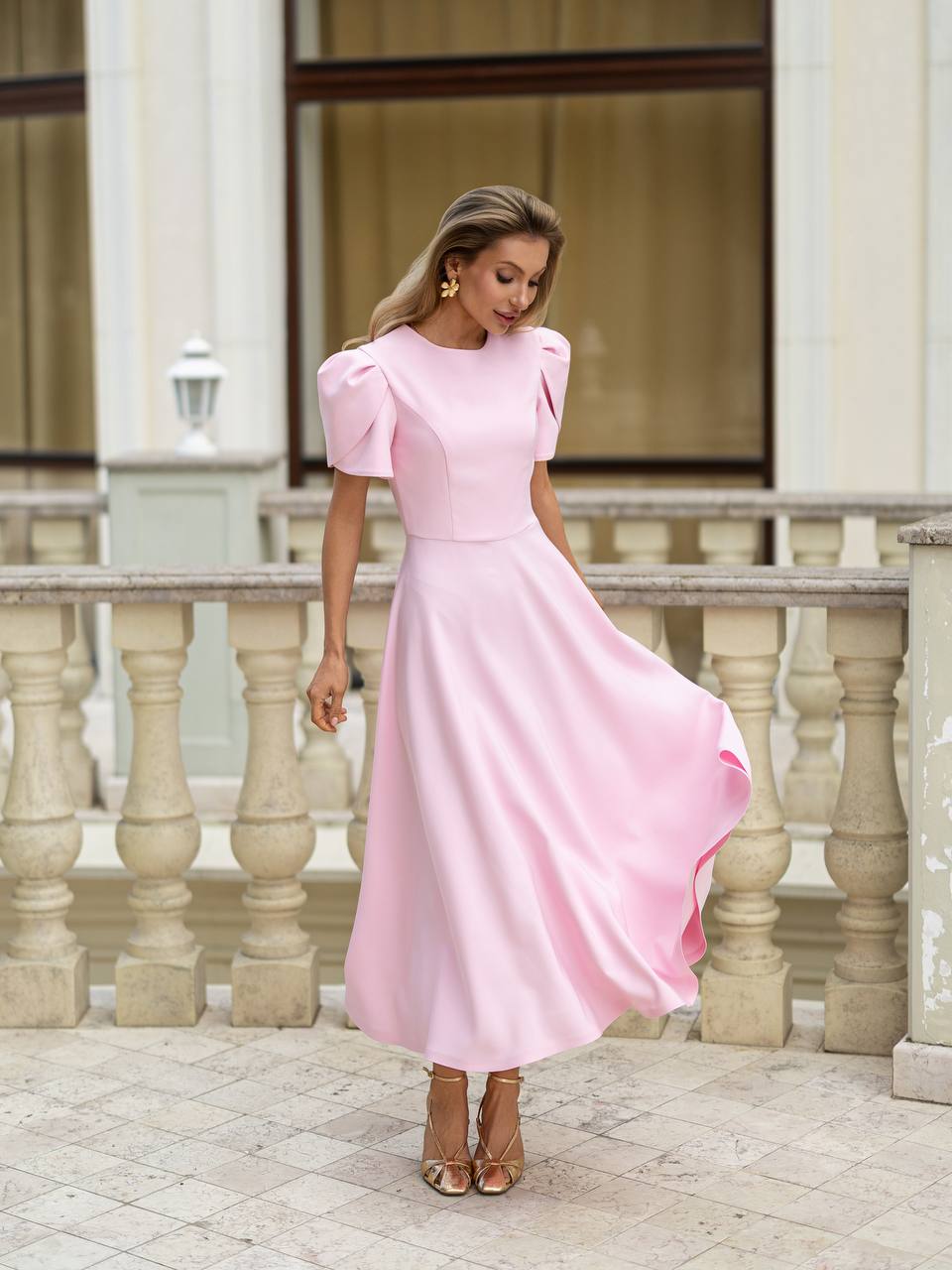 Woman in a pink dress standing on a stone pavement with classical architecture in the background