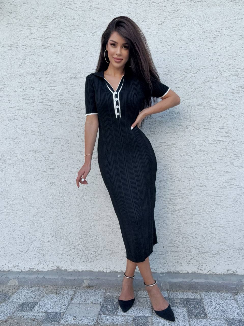 Woman wearing a black pinstripe dress against a white wall.