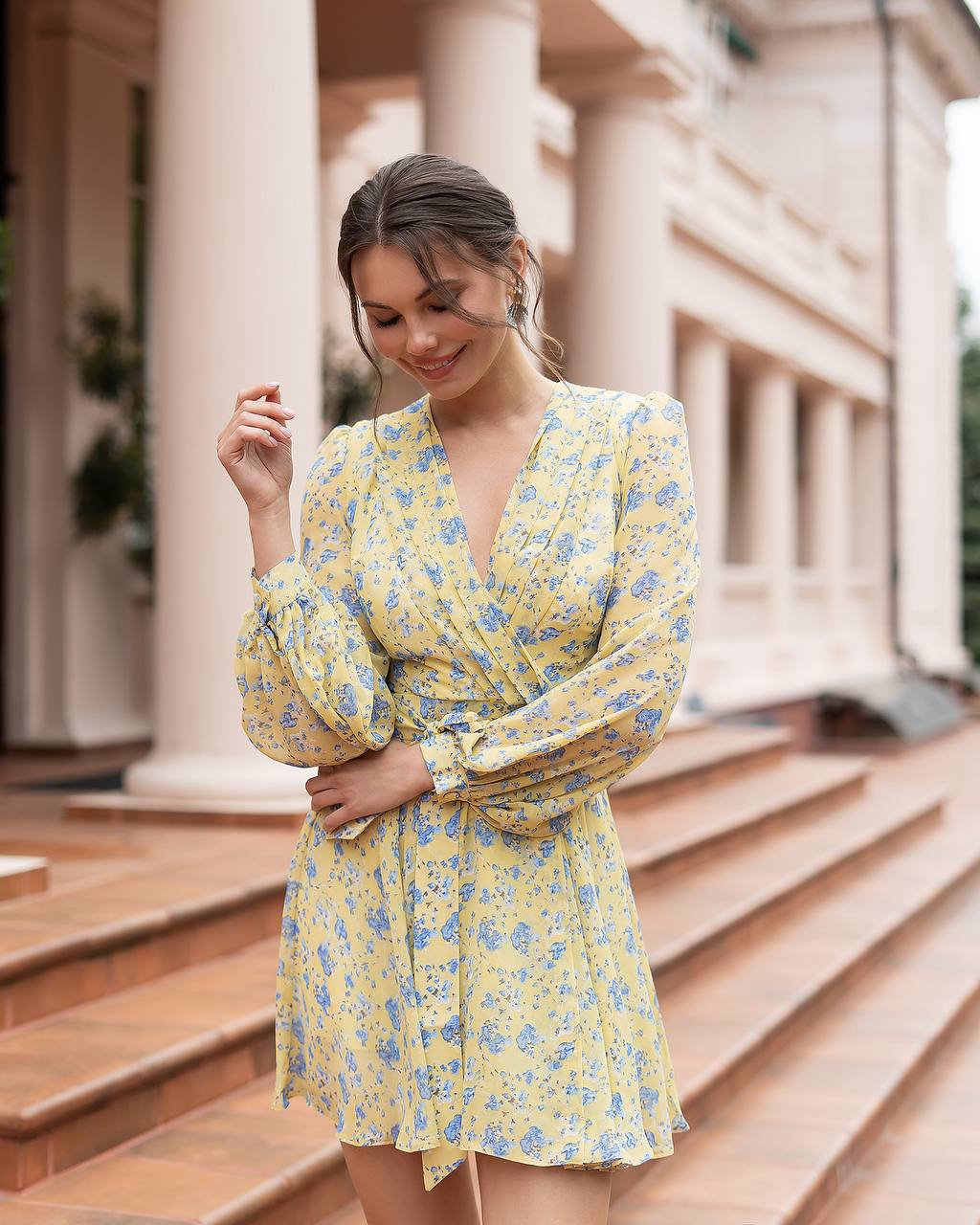 Woman in a yellow floral dress standing outdoors with classical architecture in the background
