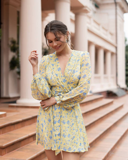 Woman in a yellow floral dress standing outdoors with classical architecture in the background