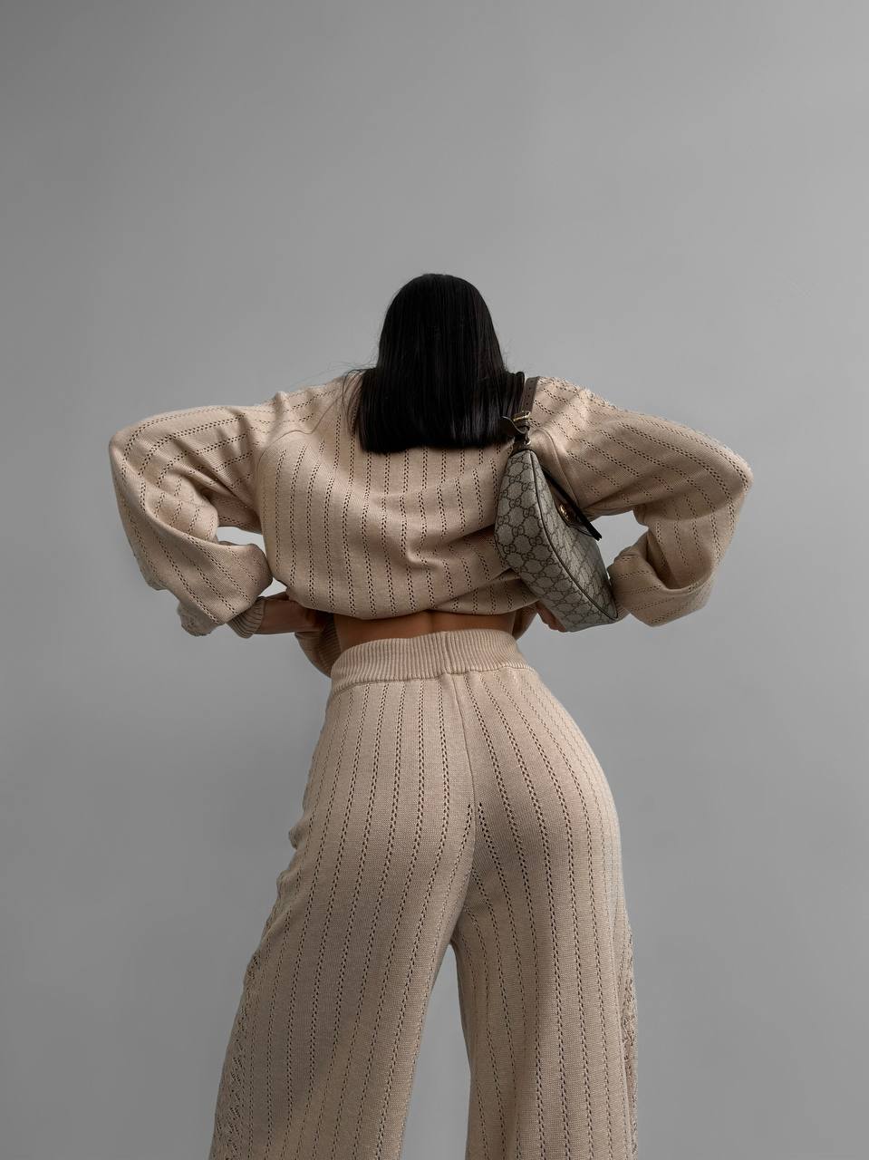 Person wearing a beige knit outfit with a gray background