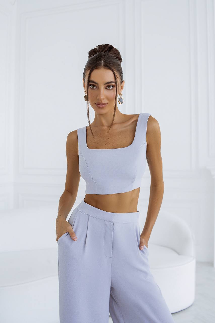 Woman wearing a light gray sleeveless top and wide-leg pants against a white background