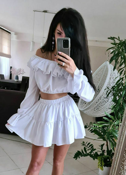 Woman taking a mirror selfie wearing a white off-shoulder top and skirt in a home setting.