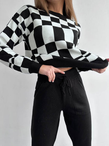 Person wearing a black and white checkered sweater with black pants on a plain background