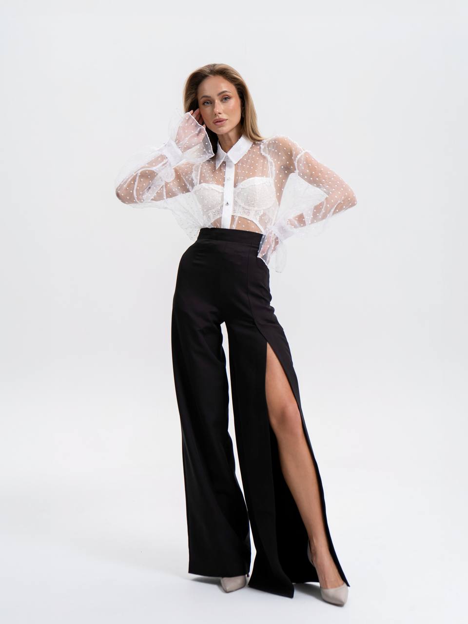 Woman wearing a white sheer blouse with a high slit black pants on a white background