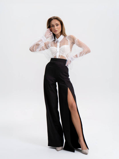 Woman wearing a white sheer blouse with a high slit black pants on a white background