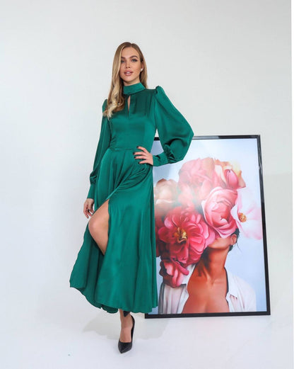 Woman in a green dress standing next to a framed artwork of a woman with flowers on her head.