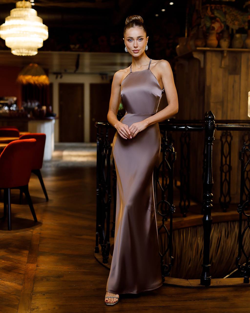 Woman in a long, elegant dress standing in an indoor setting with warm lighting.