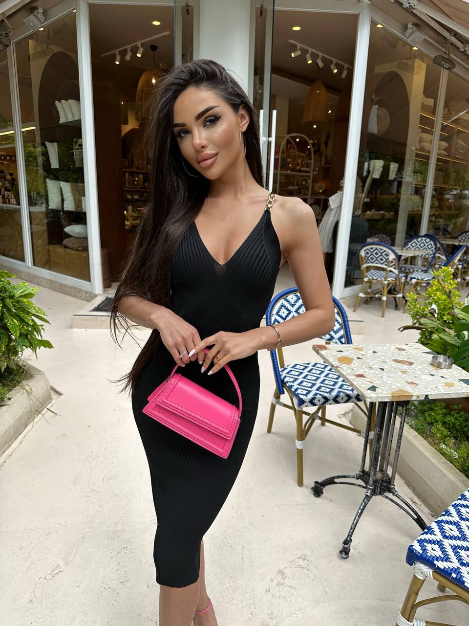 Woman in a black dress holding a pink handbag in an outdoor setting.