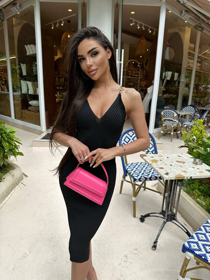 Woman in a black dress holding a pink handbag in an outdoor setting.