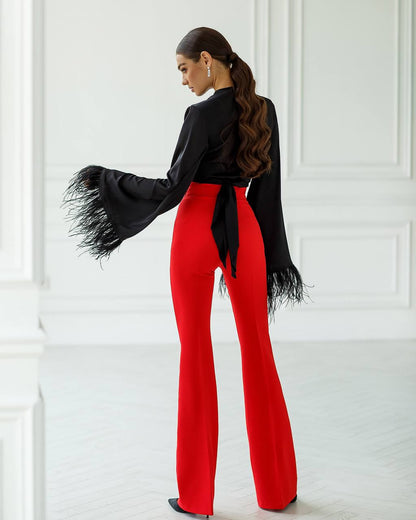 Person wearing a black top with fringes and red pants against a white wall