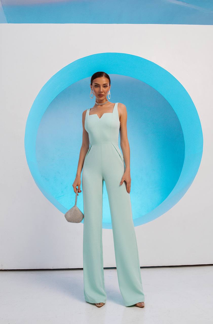 Woman in a light green jumpsuit standing against a blue circular backdrop