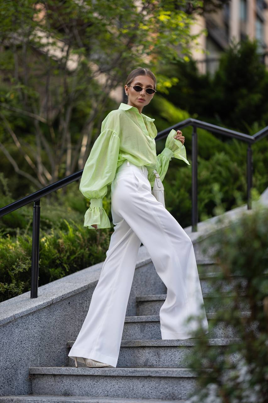 Person wearing a light green blouse and white pants on outdoor steps with greenery in the background