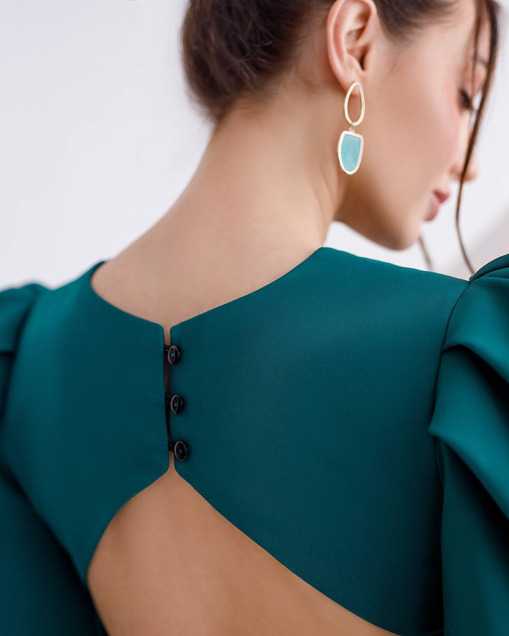 Teal dress with cut-out design and earrings on a neutral background