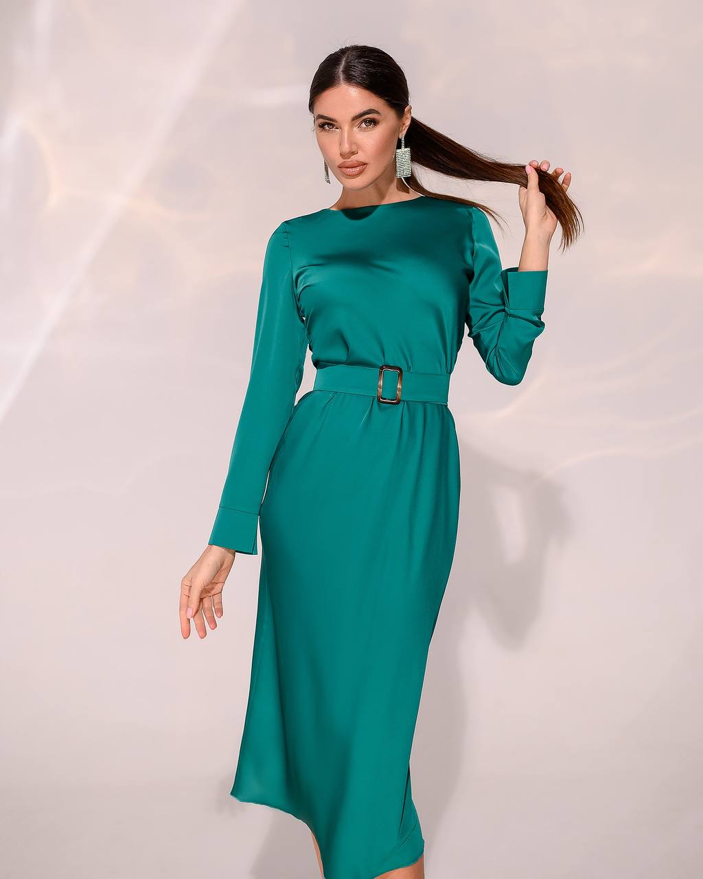Woman wearing a teal dress with a belt against a white background