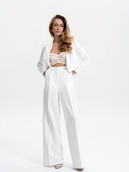 Woman wearing a white outfit with a jacket and high-waisted pants on a white background