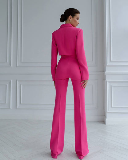 Woman wearing a bright pink suit standing in a room with white paneled walls.