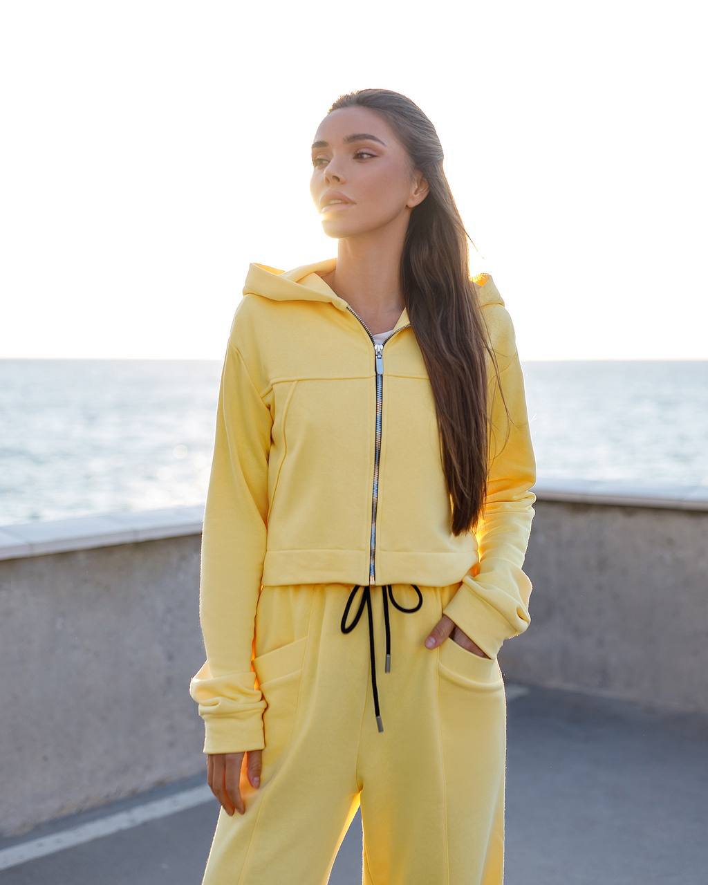 Woman wearing a yellow tracksuit standing by a waterfront.