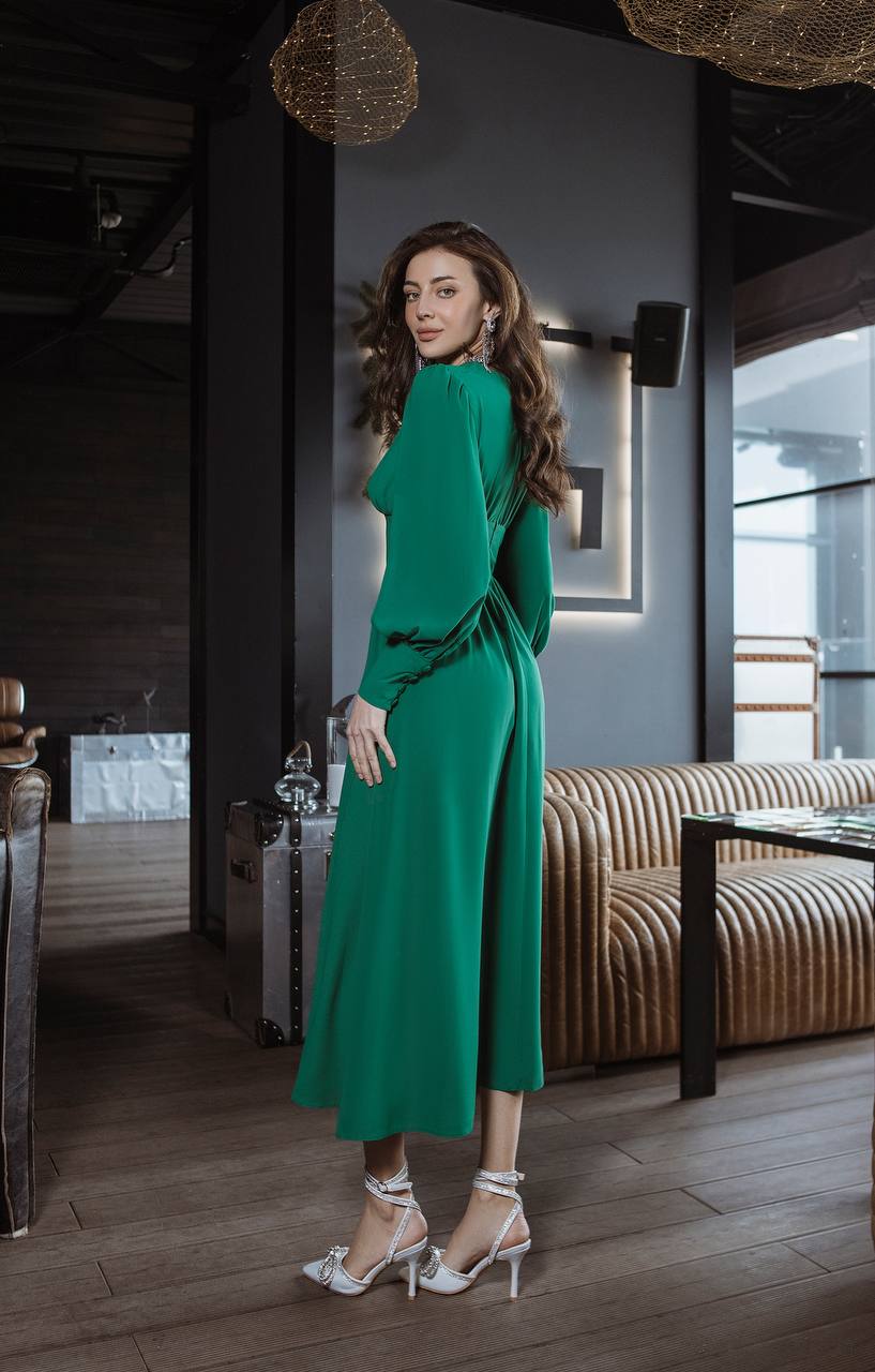 Woman in a green dress standing in an indoor setting with modern decor.