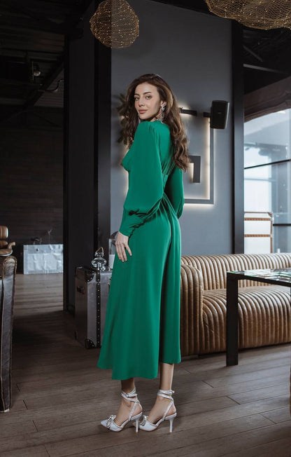 Woman in a green dress standing in an indoor setting with modern decor.