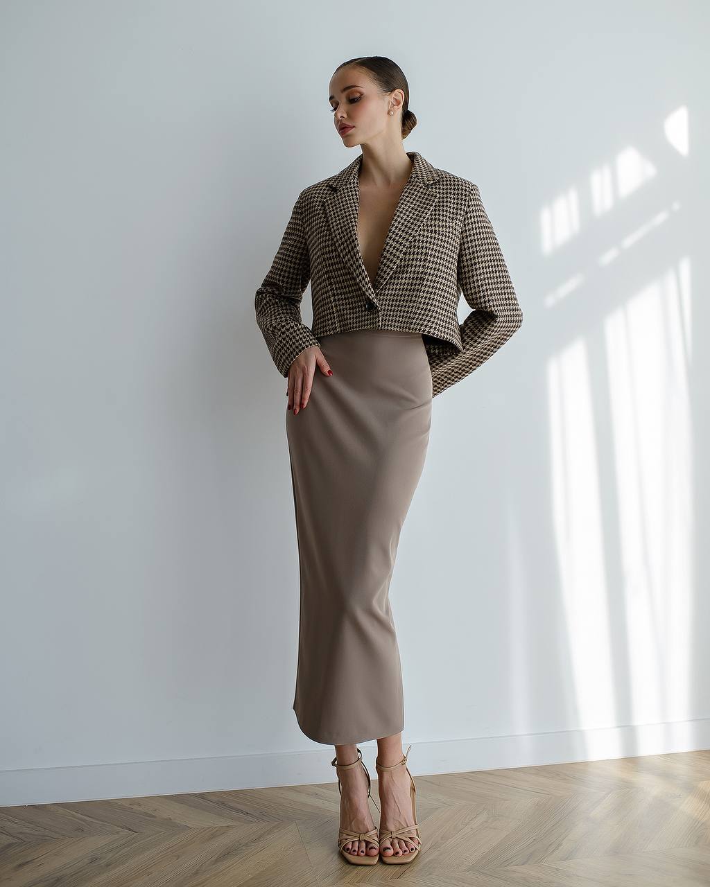 Woman wearing a brown houndstooth jacket and beige skirt in a bright room.