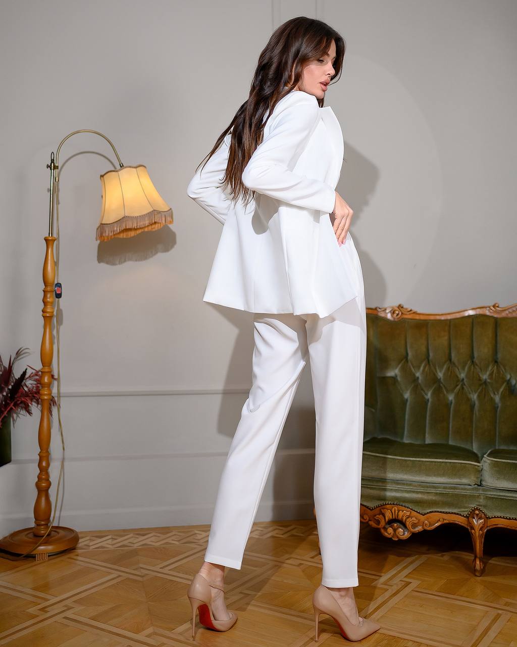 Woman in a white outfit standing in a room with a lamp and green sofa.