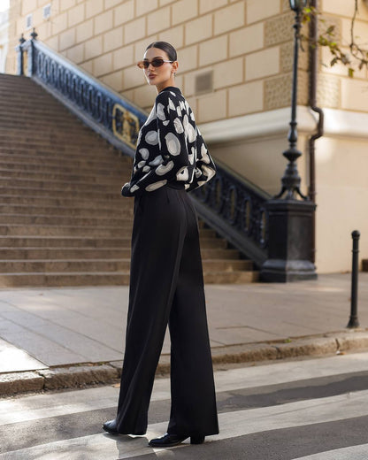 Woman in a black and white patterned top and black pants walking on a city street.