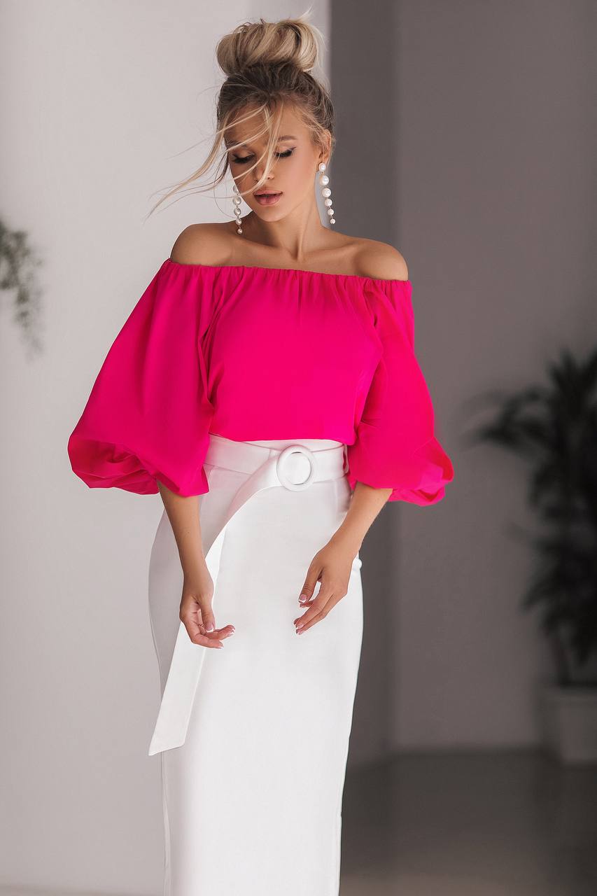 Woman wearing a bright pink off-shoulder top and white pants against a neutral background