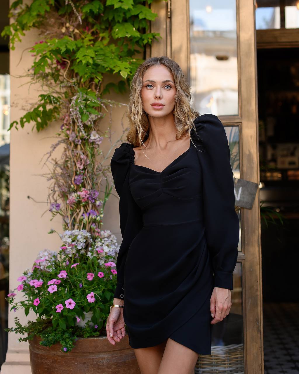 Woman in a black dress standing outdoors with plants and flowers in the background