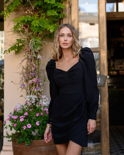 Woman in a black dress standing outdoors with plants and flowers in the background