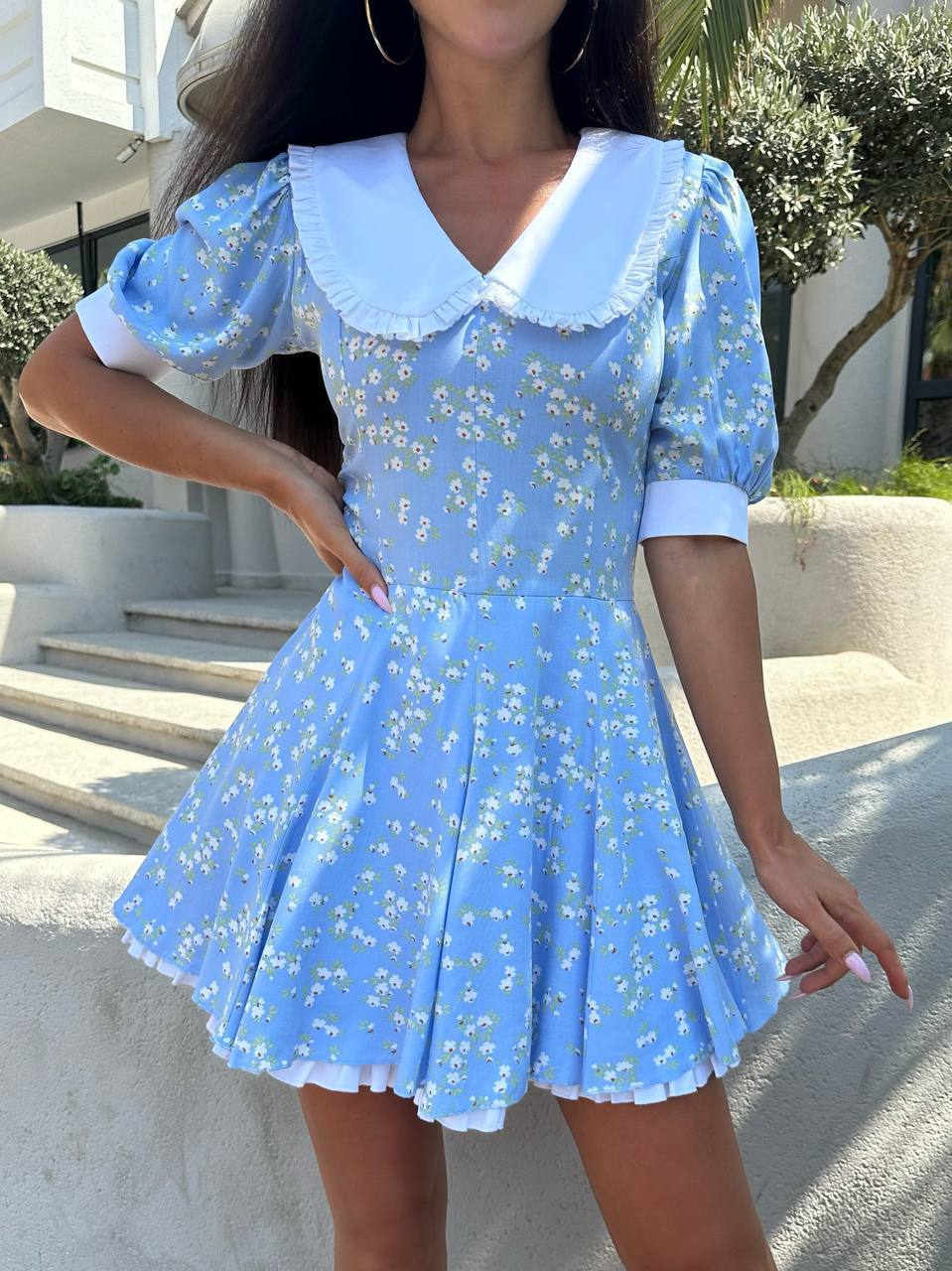 Woman wearing a blue floral dress with a white collar in an outdoor setting.