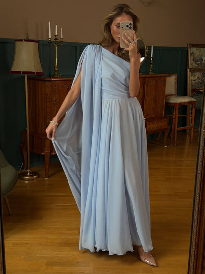 Woman in a light blue dress standing in a room with wooden floors and furniture.