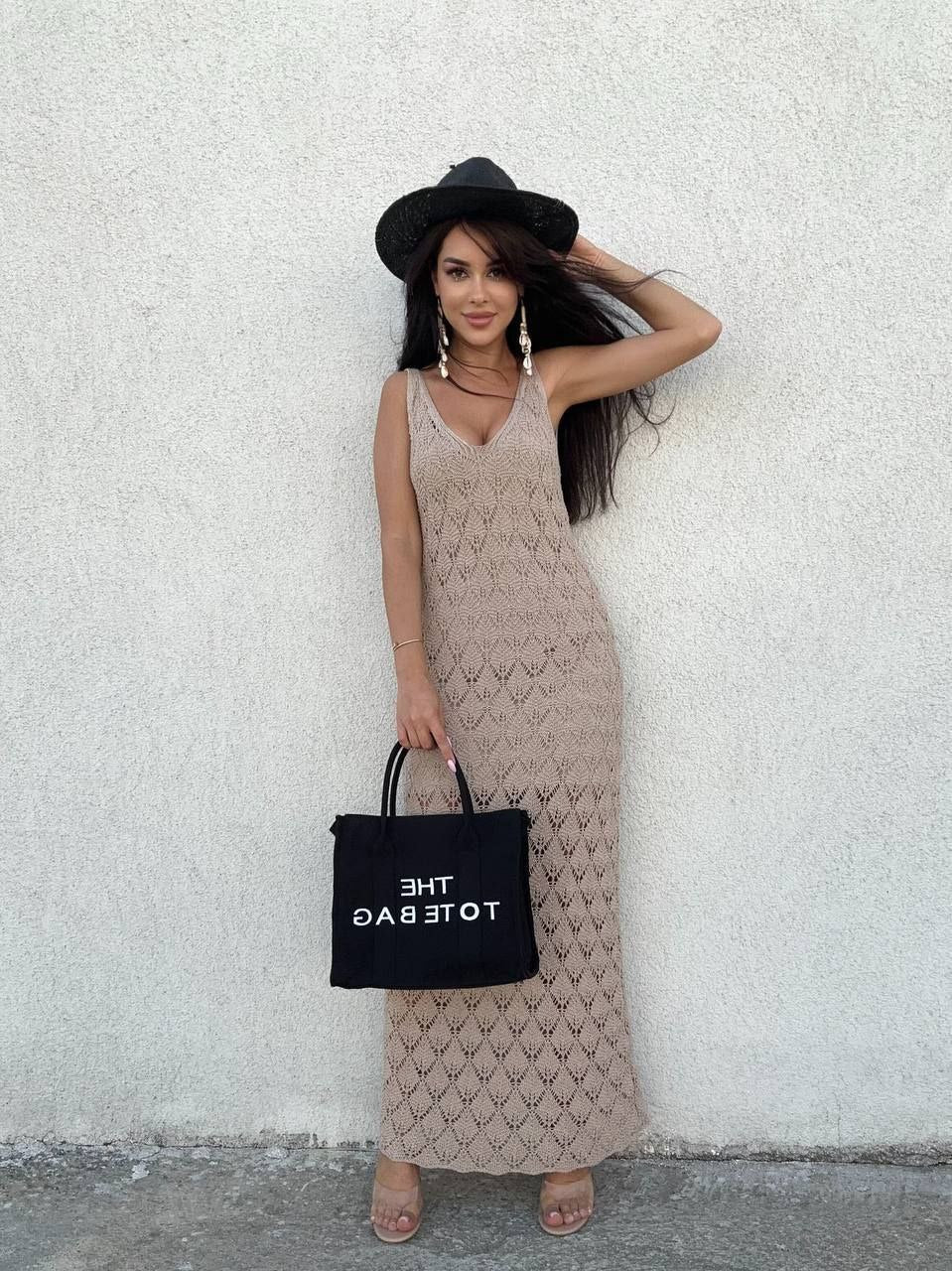 Woman in a patterned dress holding a black tote bag against a white wall