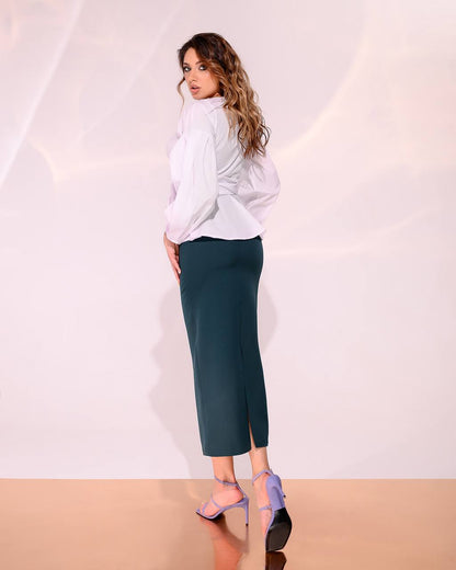 Woman wearing a white blouse and teal pants against a plain background
