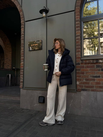 Person standing outside a building holding a cup, with a sign and window in the background.