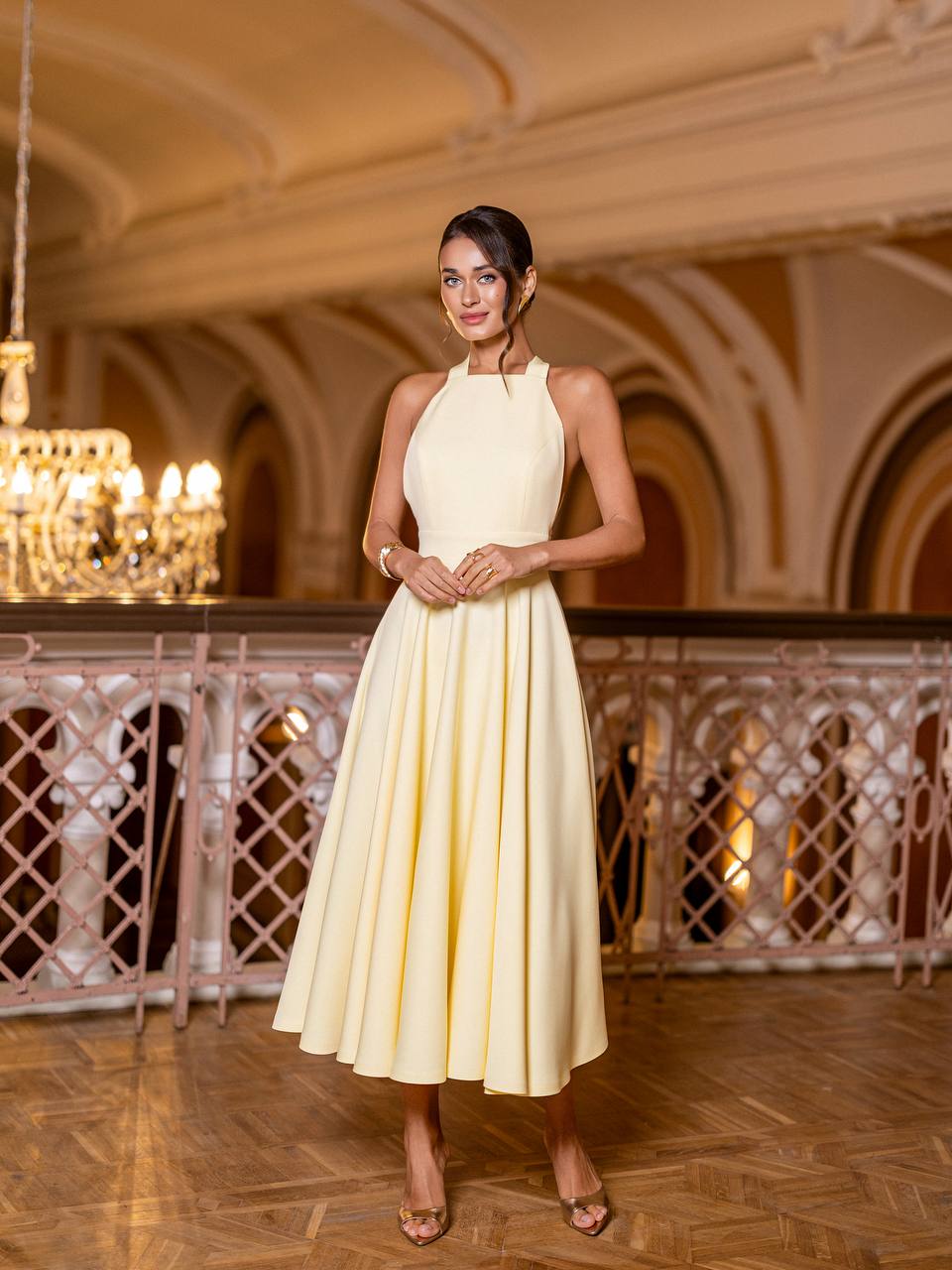 Woman in a yellow dress standing in an elegant interior setting with chandeliers.