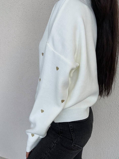 White sweater with gold heart patterns worn by a person against a plain background
