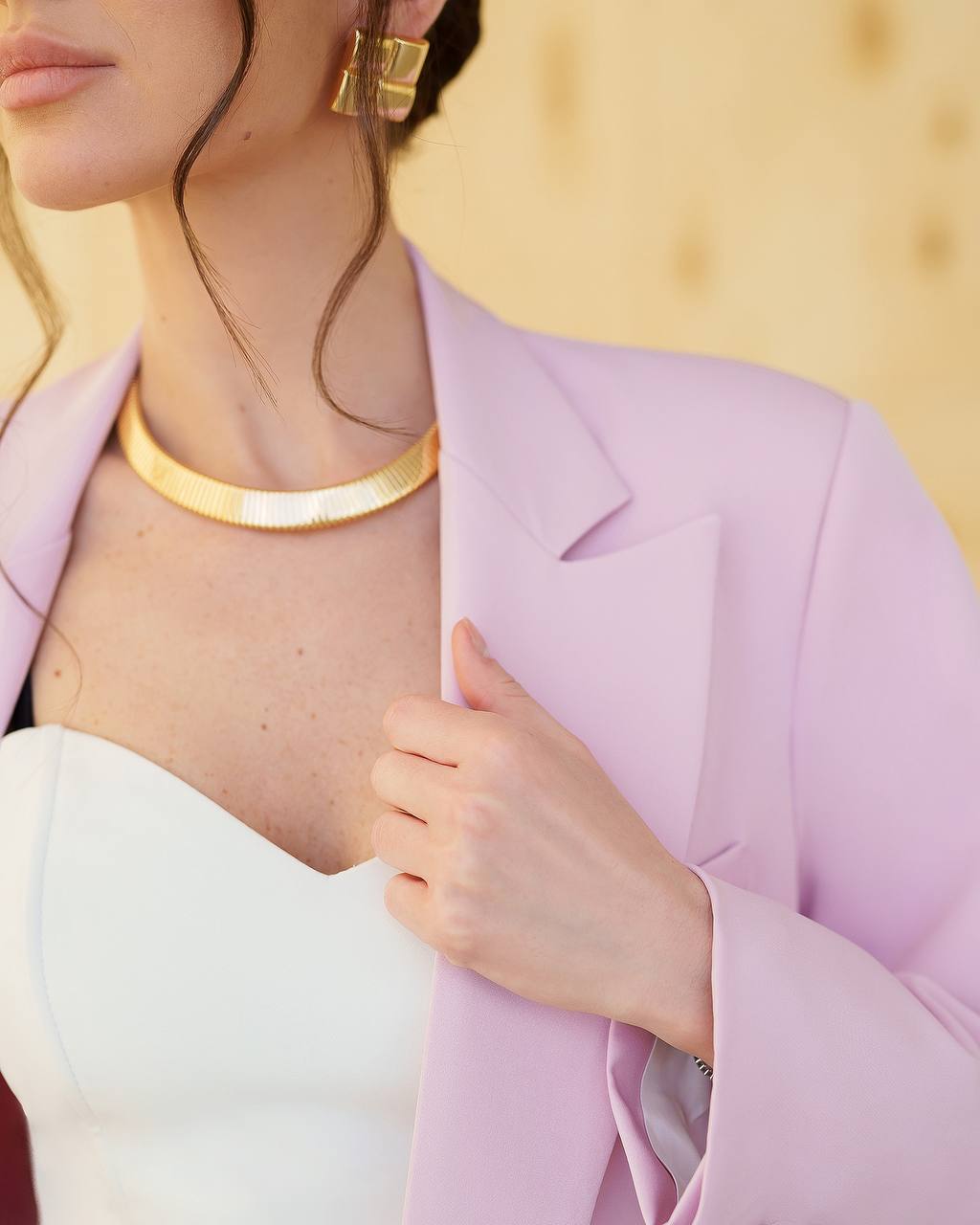 Person wearing a light purple blazer with gold jewelry against a blurred background