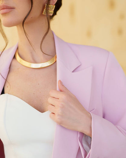 Person wearing a light purple blazer with gold jewelry against a blurred background