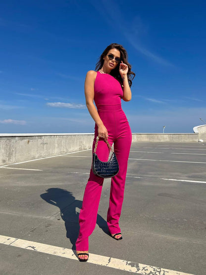 Woman in a bright pink outfit standing on a rooftop with a clear blue sky.