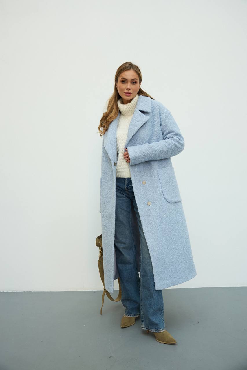 Woman wearing a light blue coat, white sweater, and jeans against a white background
