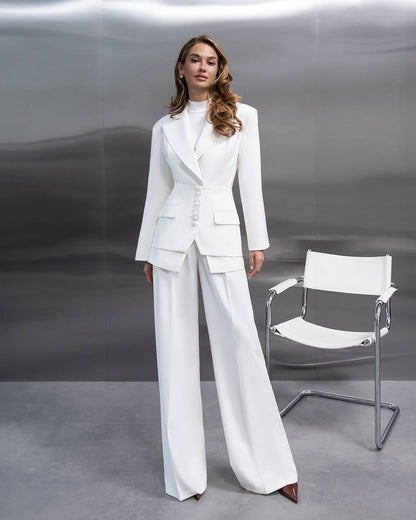 Woman in a white suit standing next to a white chair against a gray background