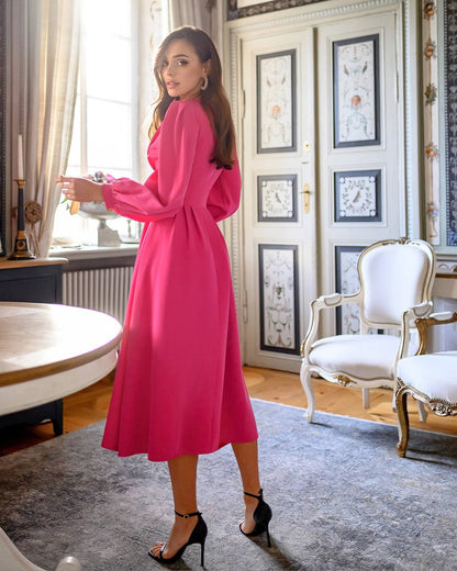 Woman in a pink dress standing in an elegant room with white chairs and framed pictures on the wall.
