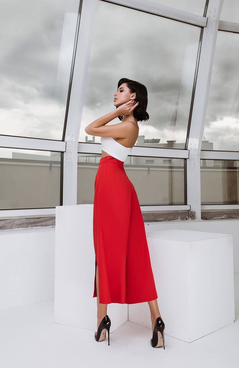 Woman in a white top and red skirt standing in front of a modern glass building.
