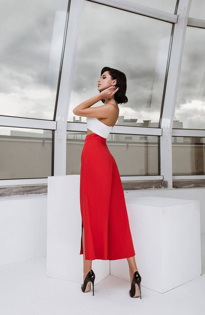 Woman in a white top and red skirt standing in front of a modern glass building.