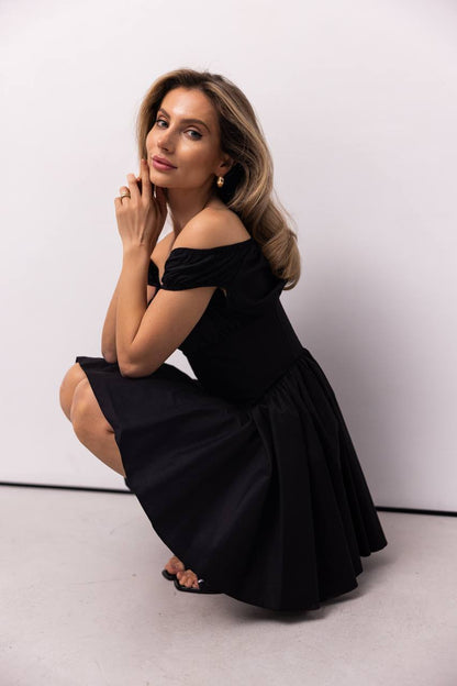 Woman in a black off-shoulder dress posing against a white background