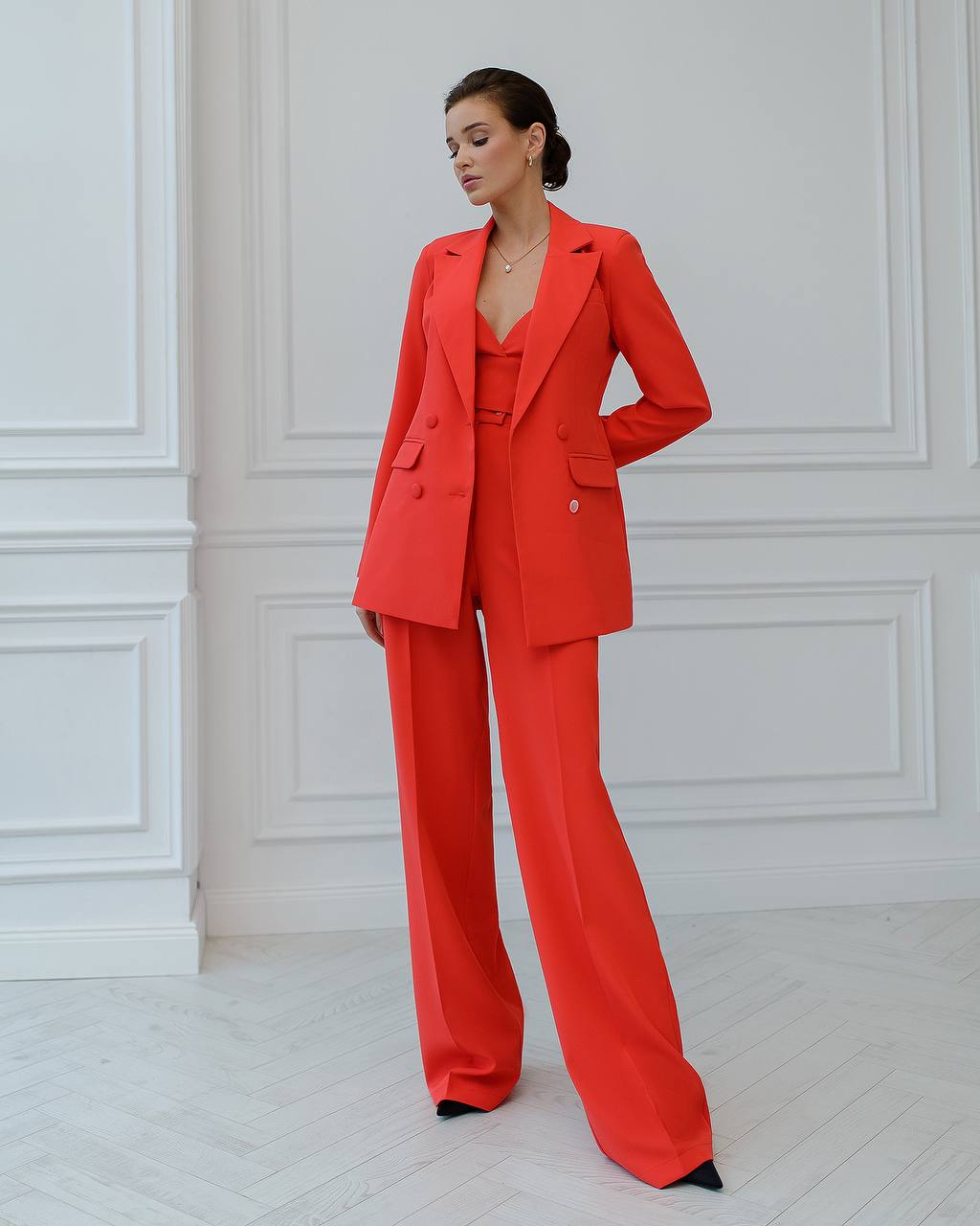 Woman wearing a red suit standing against a white paneled wall.