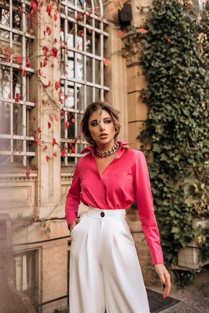 Woman wearing a pink blouse and white pants standing in an outdoor setting with ivy and red leaves.